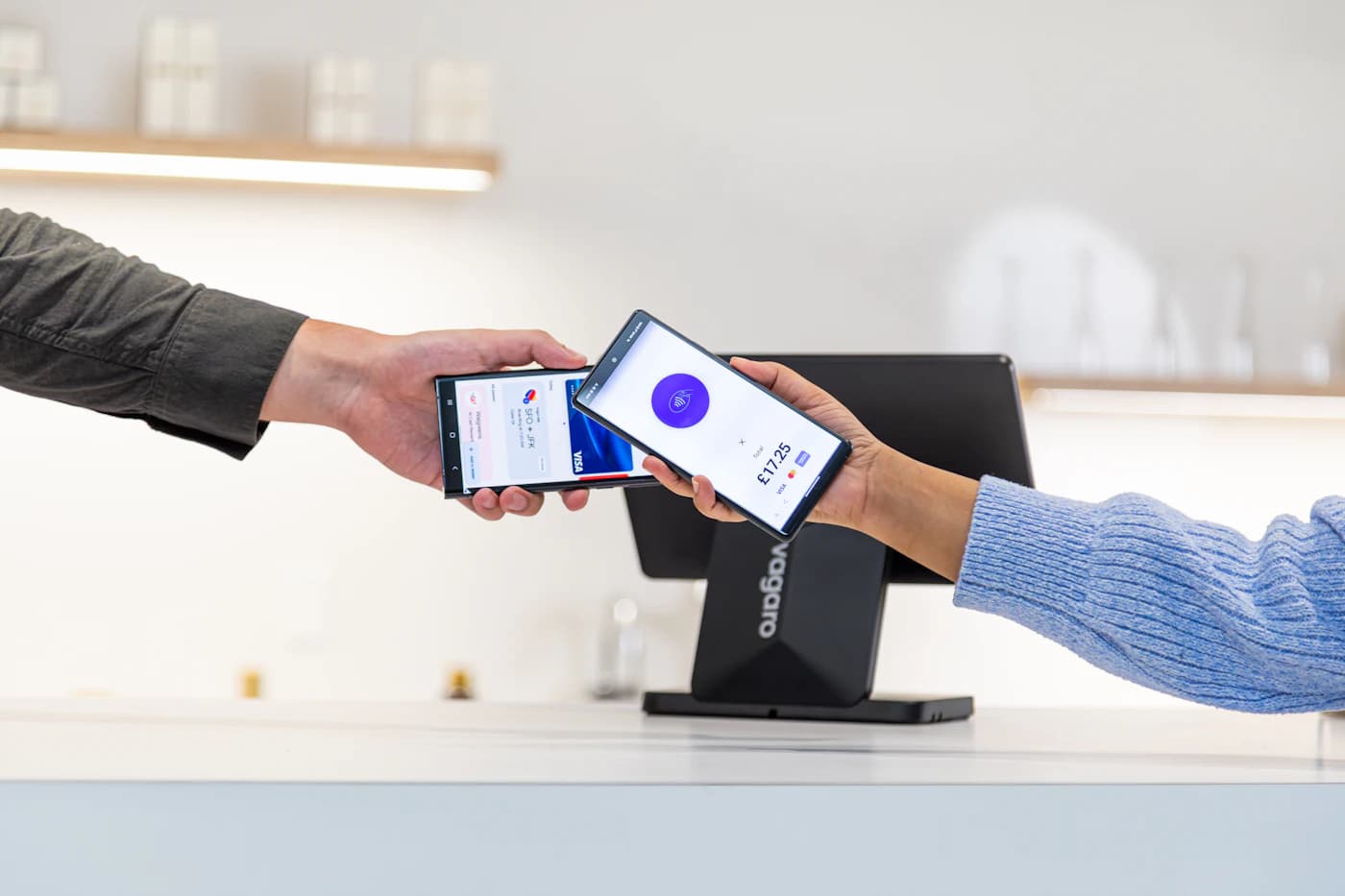 Two people exchanging phones to complete a digital payment at a retail counter.