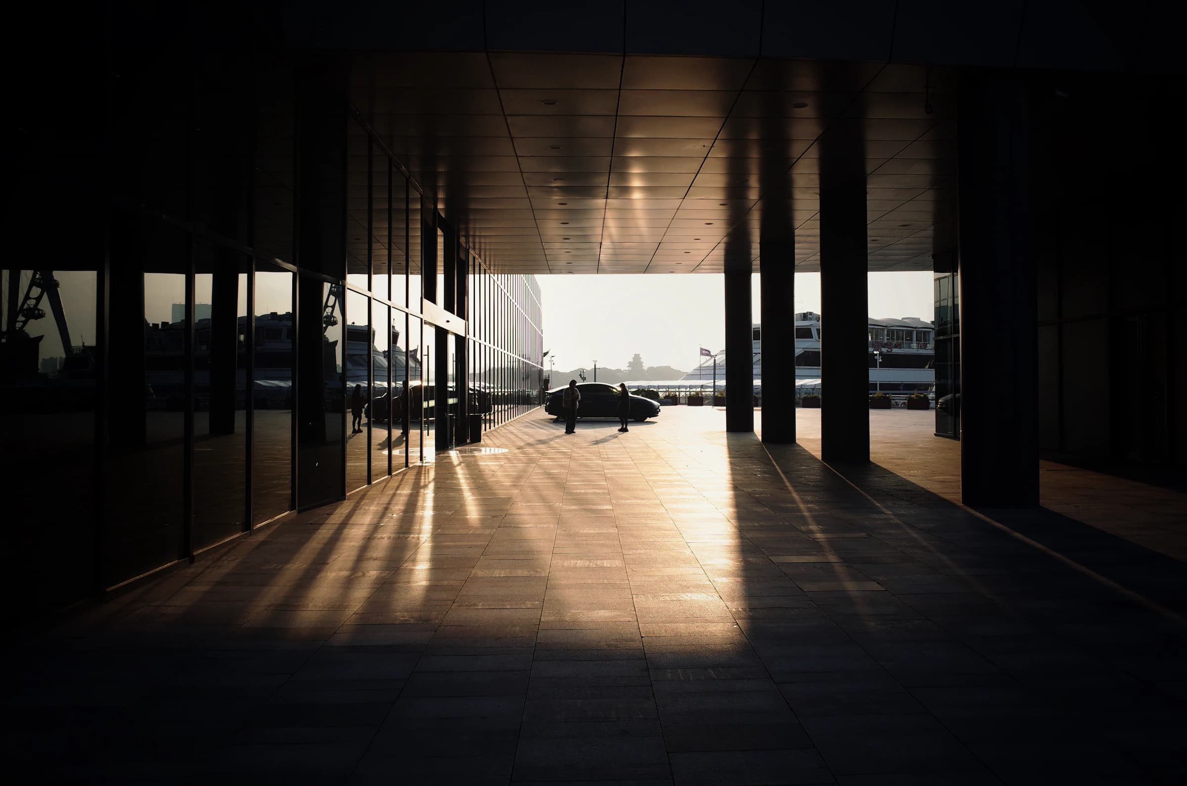 Sunlight cutting through a modern architectural walkway, casting long shadows across the floor.