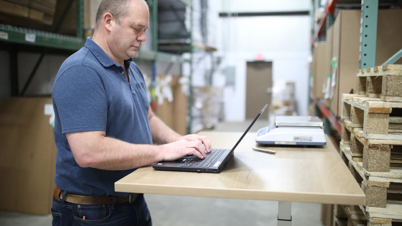 A team member working on a laptop at a standing desk inside an organized operations facility.
