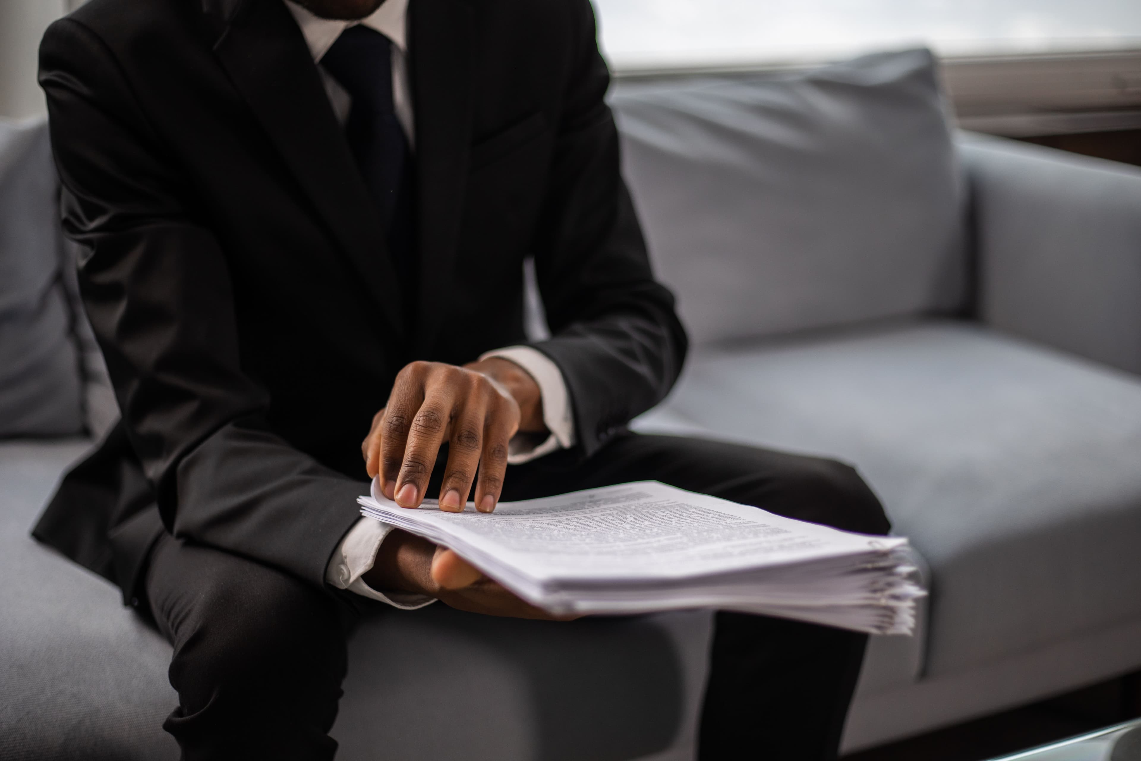 A person in a suit holding a folder of documents while seated.