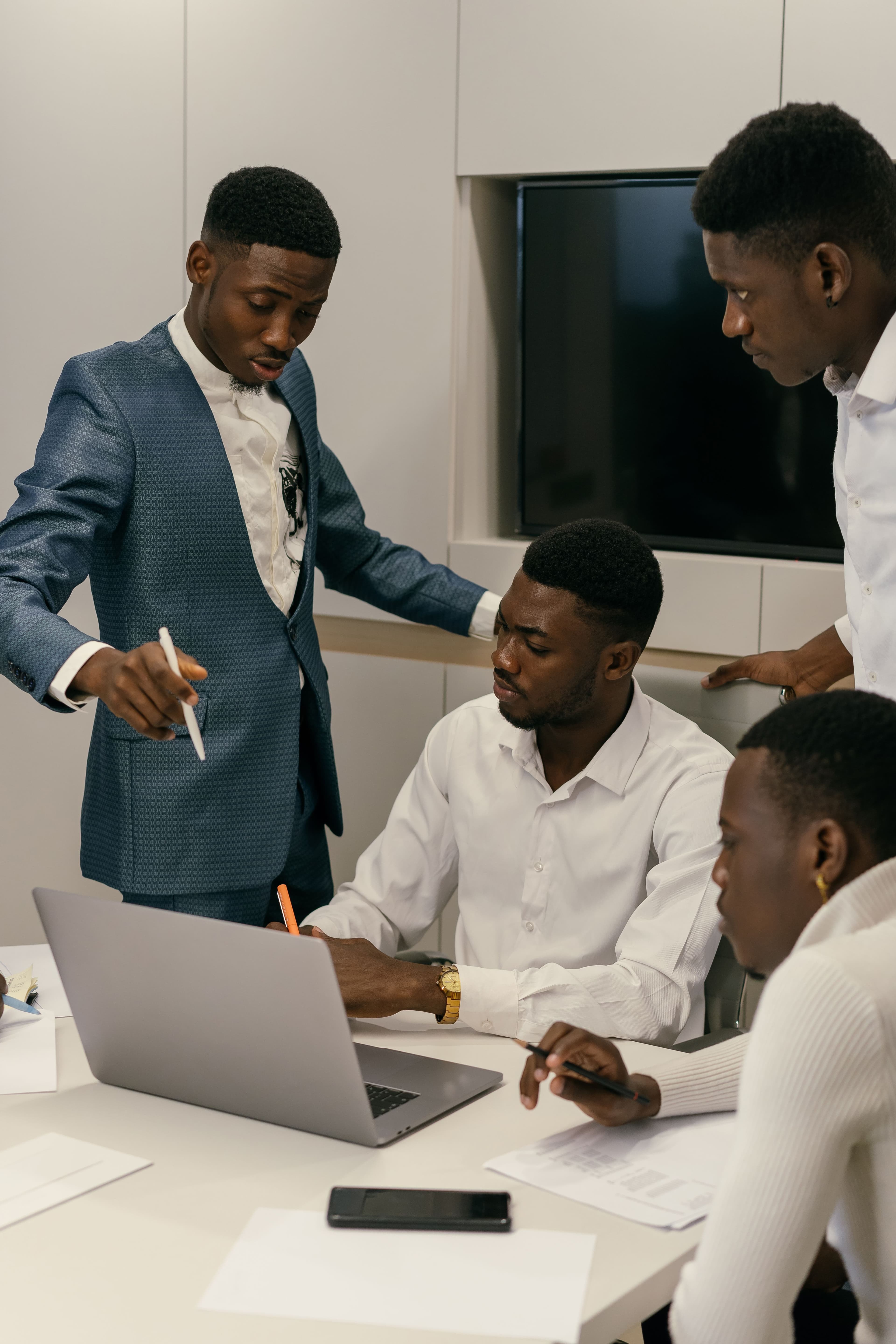 A professional standing at the head of a table, talking with seated colleagues in a bright office.