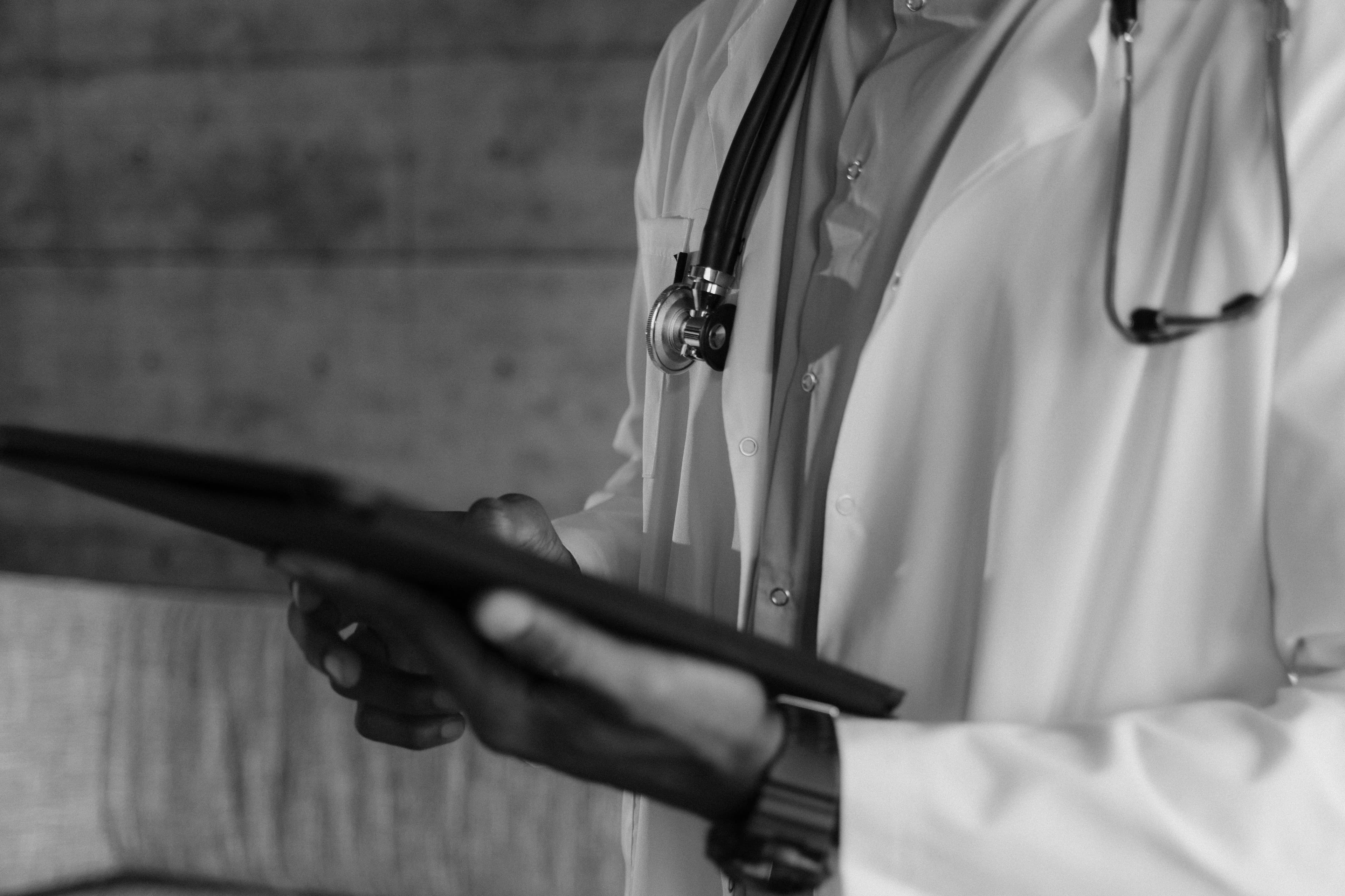 A doctor in a white coat holding a tablet, photographed in black and white.
