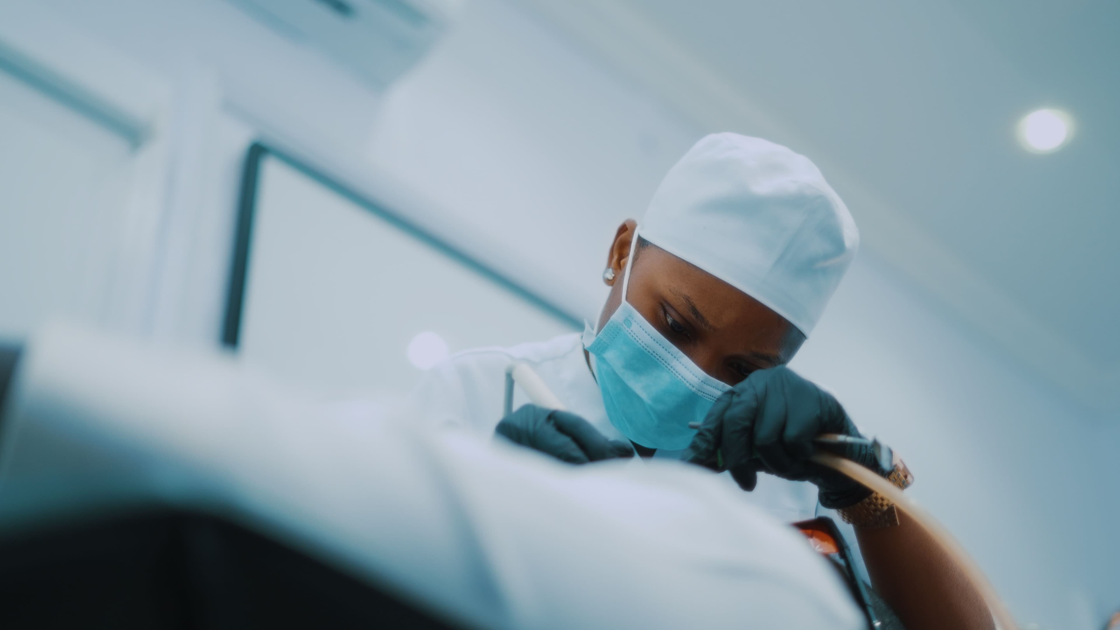 A clinician in a surgical cap and mask, looking down in concentration.